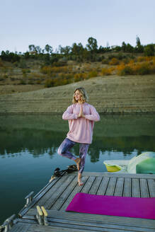 Young woman doing yoga on a jetty, tree pose - AGGF00005