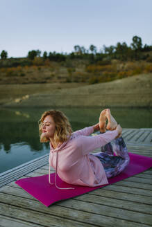 Young woman doing yoga on a jetty, bow pose - AGGF00006