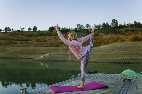 Young woman doing yoga on a jetty, dancer position - AGGF00007
