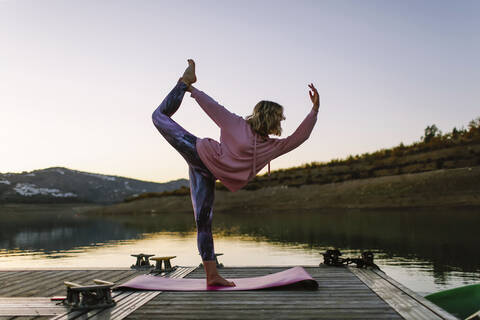 Junge Frau macht Yoga auf einem Steg, Tänzerposition, lizenzfreies Stockfoto