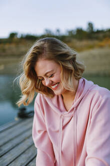 Portrait of young laughing woman wearing pink hoodie sweater on jetty - AGGF00009