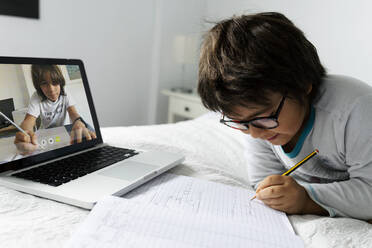 Kleiner Junge auf dem Bett liegend mit Laptop für Video-Chat - VABF02769