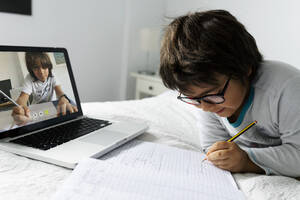 Little boy lying on bed using laptop for video chat - VABF02769