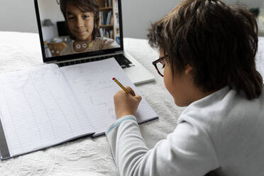 Little boy lying on bed using laptop for video chat - VABF02771