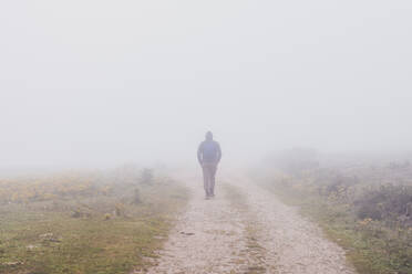 Spain, Cantabria, Silhouette of lone man walking along countryside dirt road shrouded in fog - FVSF00111