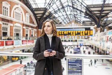 Woman at train station holding a mobile phone, London, UK - WPEF02772