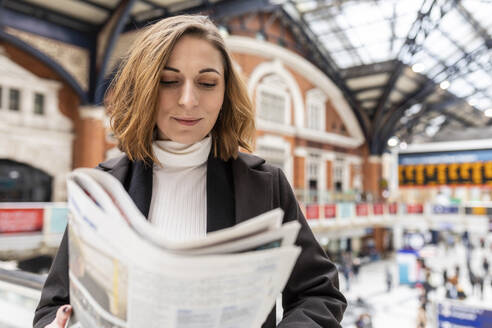 Woman at train station reading a newspaper, London, UK - WPEF02773