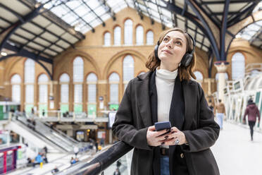 Frau am Bahnhof mit Kopfhörern und Mobiltelefon, London, UK - WPEF02777