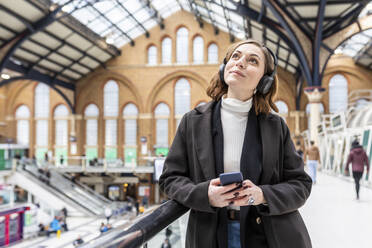 Woman at train station with headphones and mobile phone, London, UK - WPEF02777