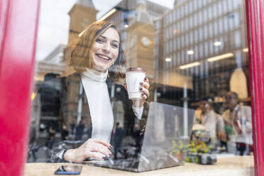 Porträt einer glücklichen Geschäftsfrau mit Laptop in einem Café in der Stadt - WPEF02786
