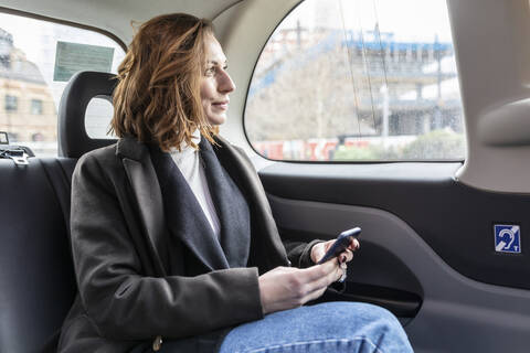 Geschäftsfrau auf dem Rücksitz eines Taxis, die aus dem Fenster schaut, London, UK, lizenzfreies Stockfoto