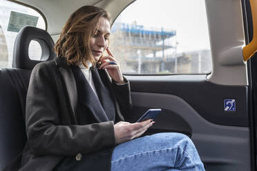 Geschäftsfrau auf dem Rücksitz eines Taxis, die auf das Telefon schaut - WPEF02793