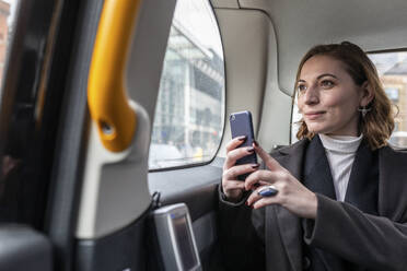 Geschäftsfrau auf dem Rücksitz eines Taxis, die aus dem Fenster schaut, London, UK - WPEF02794