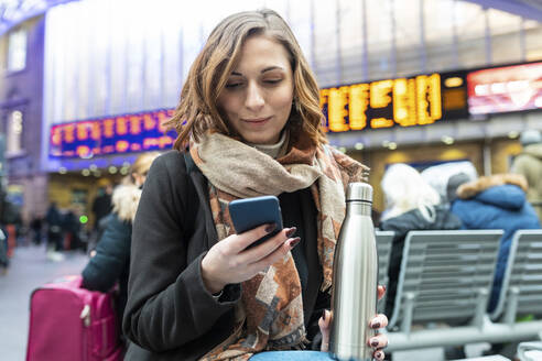 Woman sitting at train station and using mobile phone - WPEF02800