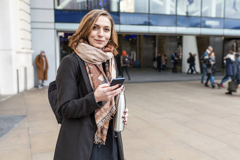 Portrait of woman with mobile phone in front of train station, London, UK - WPEF02802