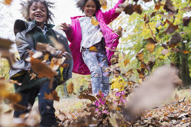 Happy brother and sister running and playing in autumn leaves - CAIF26277