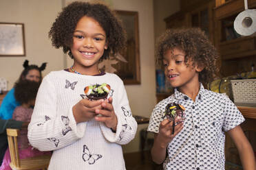 Portrait glückliche Geschwister mit dekorierten Halloween-Cupcakes - CAIF26280