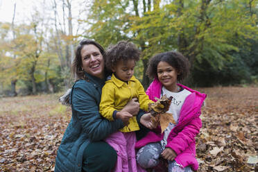 Portrait happy mother and daughters playing in autumn leaves in woods - CAIF26286