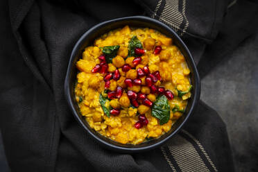 Bowl of vegan curry with red lentils, sweet potatoes, spinach, roasted turmeric chick-peas, pomegranate seeds and cilantro - LVF08787