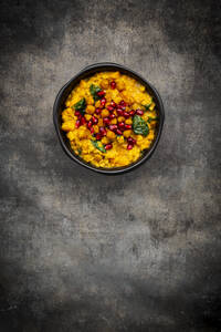 Studioaufnahme einer Schüssel mit veganem Curry mit roten Linsen, Süßkartoffeln, Spinat, gerösteten Kurkuma-Kichererbsen, Granatapfelkernen und Koriander - LVF08788