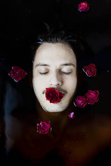 Portrait of young man with red rose in his mouth floating in water - GMLF00013