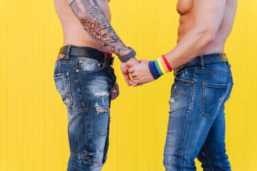 Crop-Ansicht eines schwulen Paares, das sich vor einem gelben Hintergrund die Hände hält - JCMF00574