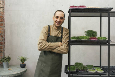 Porträt eines glücklichen Mannes, der sich an ein Regal mit Microgreens lehnt - VPIF02273