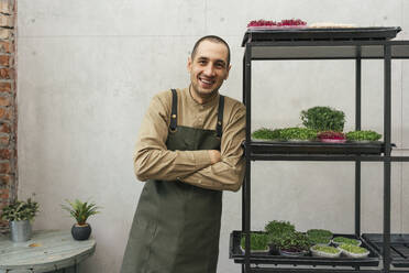 Portrait of happy man leaning against shelf with microgreens - VPIF02273