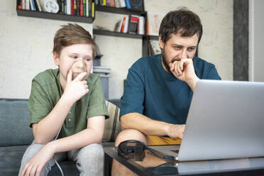 Portrait of father and son sitting together on the couch using laptop - VPIF02299