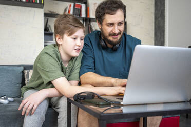 Porträt von Vater und Sohn, die zusammen auf der Couch zu Hause sitzen und einen Laptop benutzen - VPIF02301