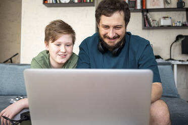 Portrait of father and son sitting together on the couch using laptop - VPIF02302