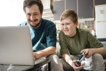 Porträt von Vater und Sohn, die zusammen auf der Couch sitzen und ein Computerspiel spielen - VPIF02306