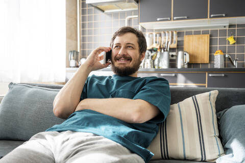Portrait of smiling man sitting on couch at home using laptop stock photo