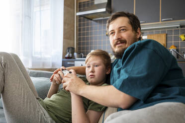 Porträt von Vater und Sohn, die zusammen auf der Couch sitzen und ein Computerspiel spielen - VPIF02315