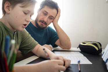 Portrait of father watching his son doing homework - VPIF02317
