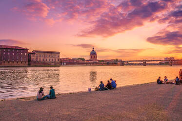 Menschen sitzen am Fluss gegen dramatischen Himmel bei Sonnenuntergang - EYF03779