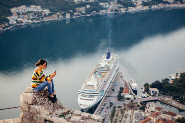 Seitenansicht der Mid Adult Frau mit Handy während des Sitzens auf einem Felsen gegen das Meer - EYF03828