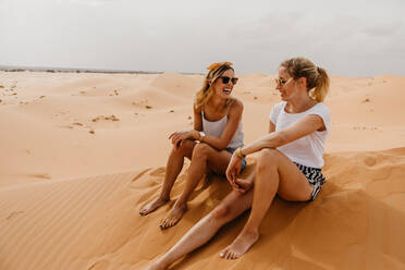 Fröhliche Freunde sitzen auf Sand in der Wüste gegen den Himmel - EYF03924