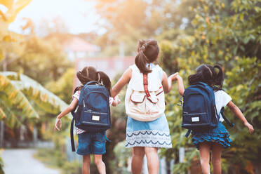 Rear View Of Girls With Backpacks Holding Hands While Walking On Road - EYF03936