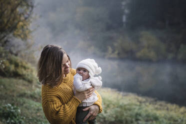 A woman is holding a baby near a river - CAVF79043