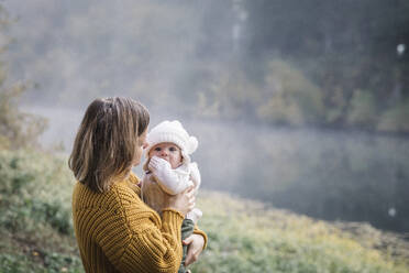 A woman is holding a baby near a river - CAVF79057