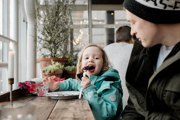 Vater und Tochter essen gemeinsam Schokoladenkuchen in einem Cafe - CAVF79060