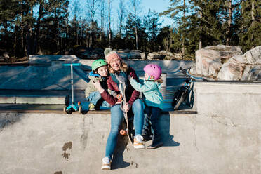 Mom and her kids having fun in a skatepark with bikes and scooters - CAVF79063