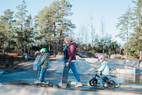 Mutter und ihre Kinder gehen über einen Skatepark, um zu fahren und Spaß zu haben - CAVF79064