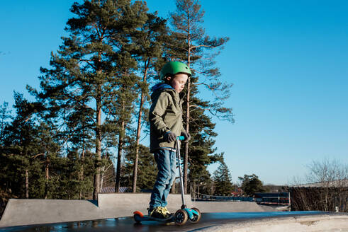 Junge steht auf seinem Roller in einem Skatepark in der Sonne - CAVF79066