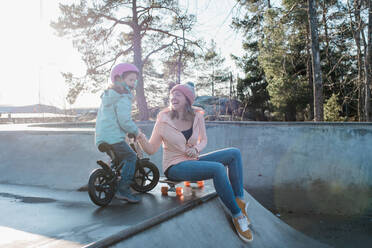 Mom and daughter playing and laughing in a skatepark in the sun - CAVF79068
