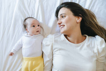 Woman and baby girl lying in bed looking at each other - KIJF02965