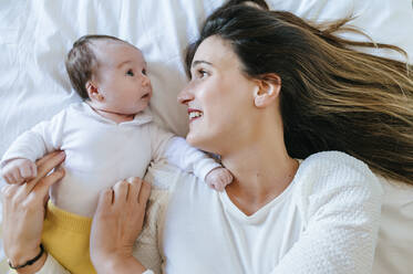Woman and baby girl lying in bed looking at each other - KIJF02966