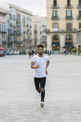 Porträt eines lachenden jungen Mannes, der auf einem Platz läuft, Barcelona, Spanien - XLGF00021