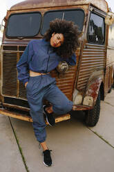 Porträt einer stilvollen jungen Frau im Trainingsanzug, die sich an einen alten Lieferwagen lehnt - AGGF00018